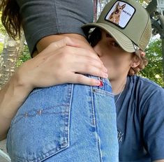 a woman wearing a hat and jeans is hugging another woman's back with her hand on her hip