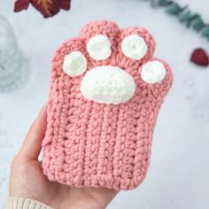 a hand holding up a pink crocheted cell phone case with white paws on it