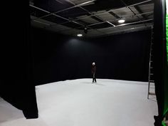 a person standing in an empty room with black curtains on the walls and lights hanging from the ceiling