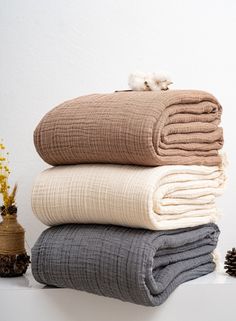 three blankets stacked on top of each other in front of a white wall and pine cones