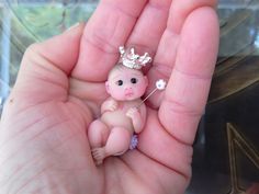 a tiny baby doll with a crown on it's head in someones hand