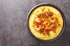 a bowl filled with shrimp and grits on top of a gray table next to a fork