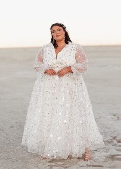 a woman wearing a white dress standing in the sand with her hands on her hips