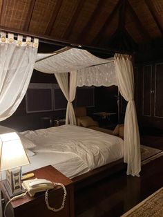 a bed with white sheets and drapes on it's headboard in a bedroom