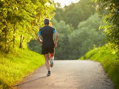 a man running down a dirt road in the middle of some trees and grass with his back turned to the camera