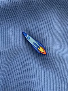 a pin with a rocket ship on it sitting on top of a blue shirt that is rolled up