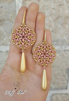 a pair of pink and gold earrings on someone's hand with stone work in the middle