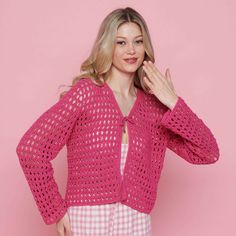 a woman wearing a pink crochet cardigan standing in front of a pink background