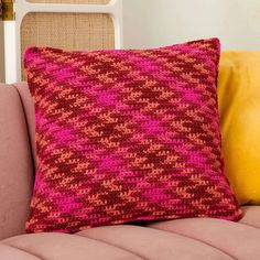 a pink and red pillow sitting on top of a couch next to two yellow pillows