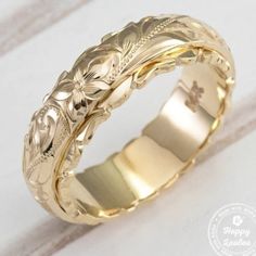 a yellow gold wedding ring with an intricate design on the outside and inside, sitting on a white surface