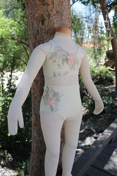 a white mannequin standing next to a tree in front of a wooden walkway