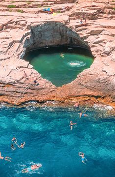 people swimming in the blue water near some rocky cliffs and an opening to a cave