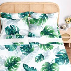 a bed with green leaves on it in a room next to a nightstand and table