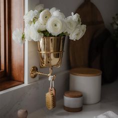 white flowers are in a gold vase on the counter next to a brush and soap dispenser