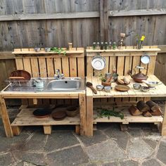 an outdoor kitchen made out of pallets and wooden planks with pots, pans, plates and utensils on it