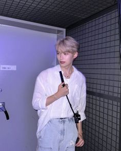 a young man holding a hair dryer while standing in front of a wall with grids on it