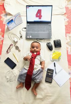 a baby doll with a red tie laying on top of a bed next to a laptop