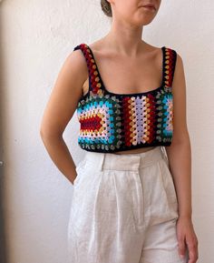 a woman standing in front of a white wall wearing a colorful crochet top