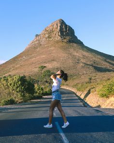 a woman is walking down the road in front of a mountain