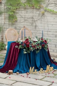 the table is set up with blue and red linens, gold letters, greenery and candles