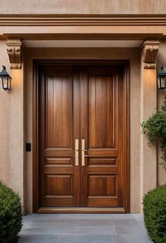 a large wooden door in front of a house with two lights on each side and green bushes next to it