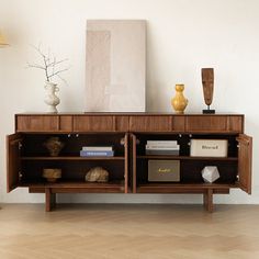 a sideboard with books and vases on it in a room that has hard wood flooring