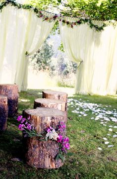 an outdoor ceremony with wooden logs and flowers on the grass in front of white drapes