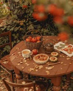 a wooden table topped with apples and pies next to a basket filled with leaves