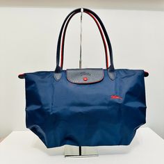 Longchamp Le Pliage Medium Nylon And Leather Tote Bag Limited Edition Style. Product Details: Nylon And Leather Navy And Red Foldable Handle/Strap: Double Rolled Handle With 8" Drop Dimension: 18" (W) X 12" (H) Size: Medium Le Pliage Medium, Longchamp Le Pliage Medium, Longchamp Bags, Medium Tote, Longchamp Le Pliage, Leather Tote Bag, Womens Tote Bags, Limited Editions, Leather Tote