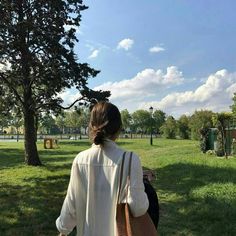 a woman is walking in the park with her back turned to the camera, carrying a brown bag