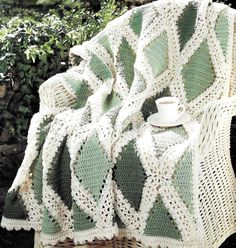 a white and green crocheted blanket sitting on top of a wicker chair