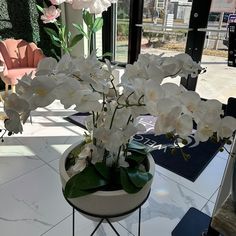 a vase with white flowers on a table in front of a large glass window,