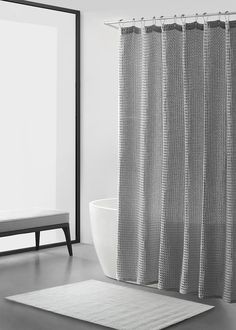 a white bath tub sitting next to a shower curtain on a bathroom floor near a mirror