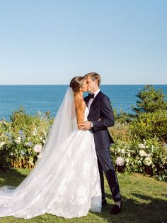 a bride and groom kissing in front of the ocean