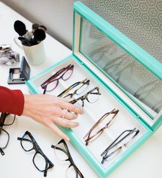 a person's hand reaching for glasses in a display case on a white table