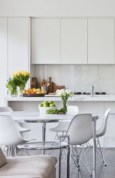 a kitchen with white cabinets and chairs around a dining table that has fruit on it