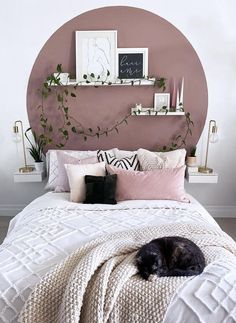 a black cat laying on top of a white bed next to a pink circle wall