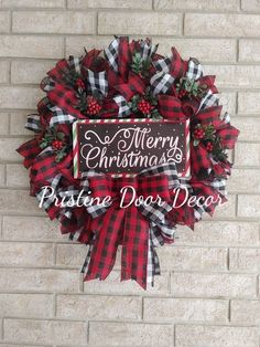 a red and black christmas wreath hanging on the side of a brick wall next to a sign