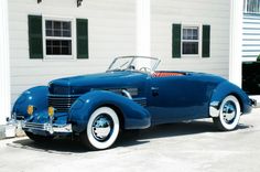 an old blue car parked in front of a white house