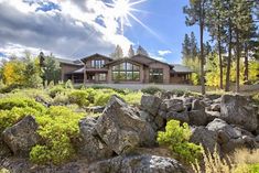 a house surrounded by rocks and trees on a sunny day with the sun shining through the clouds