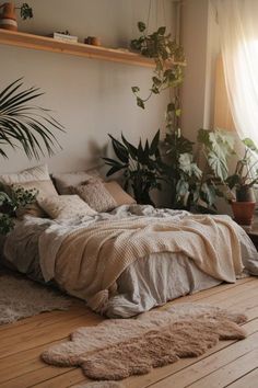 an unmade bed with lots of plants in the corner