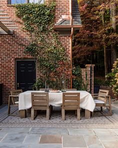 an outdoor dining table with four chairs and a white table cloth on it in front of a brick building