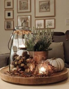 a table topped with a glass vase filled with plants and candles on top of a wooden tray