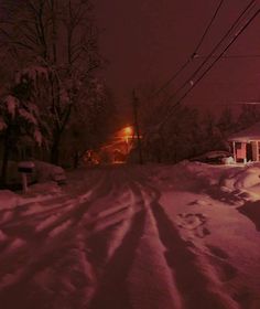 a snow covered street at night with power lines in the distance and houses on the other side