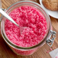 a jar filled with pink colored sugar next to two muffins on top of a wooden table