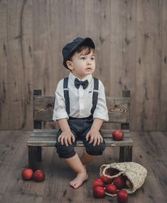 a little boy sitting on a wooden bench next to apples