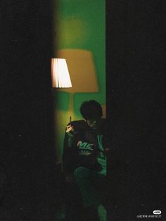 a man sitting in front of a lamp next to a green wall with a white light on it