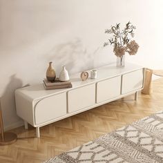 a white dresser with vases and flowers on it in the corner of a room