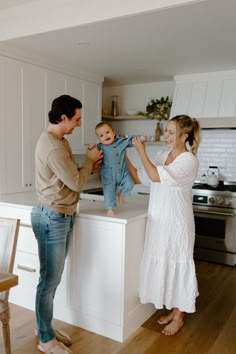 a man and woman holding a baby while standing in front of a kitchen counter top