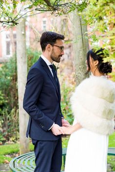 a man and woman standing next to each other in front of a tree on a bench